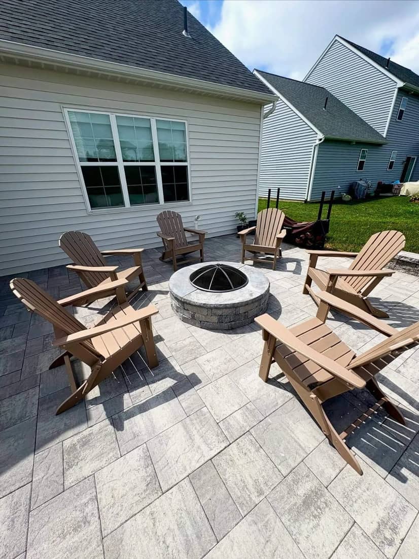 Circular stone fire pit surrounded by Adirondack chairs on a paver patio
