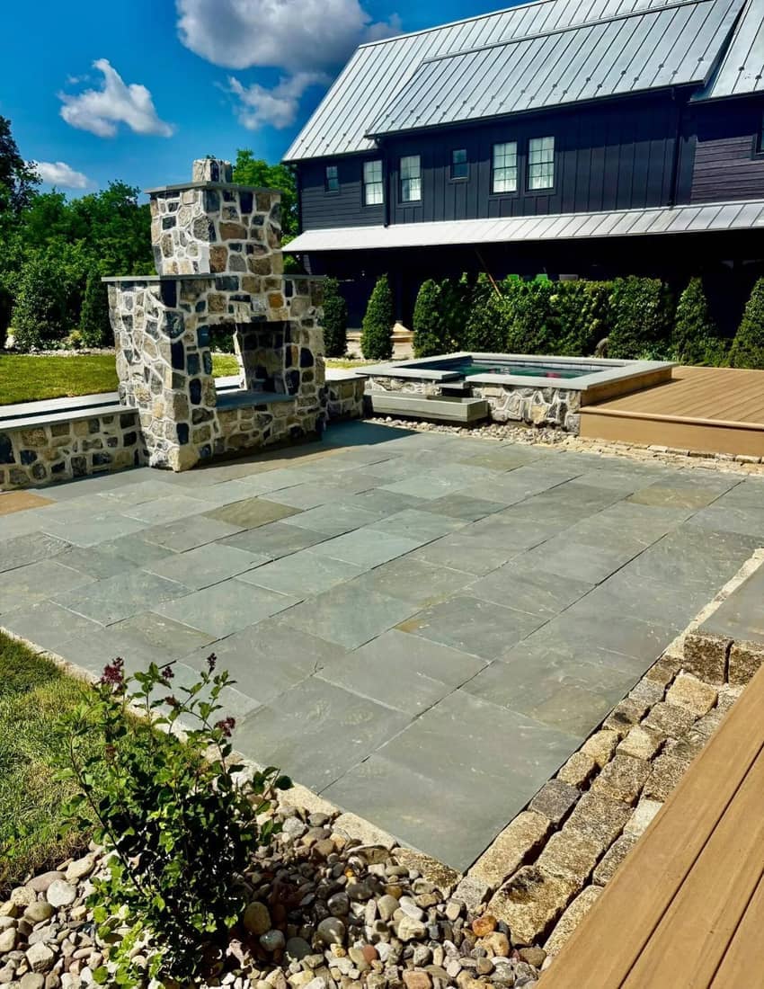 Large natural-stone patio with a stone outdoor fireplace and spa