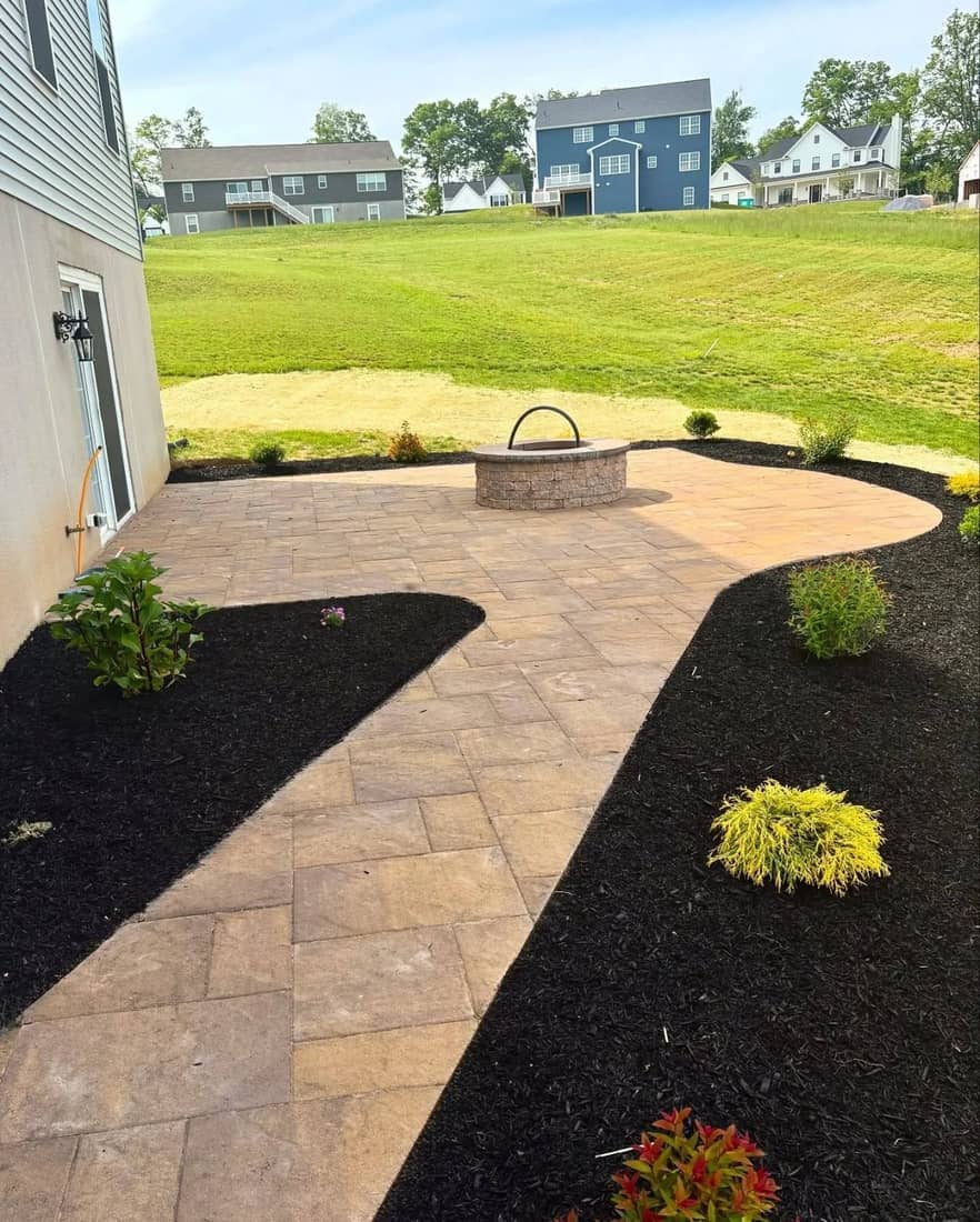 Curved tan paver patio with a fire pit and mulched planting beds