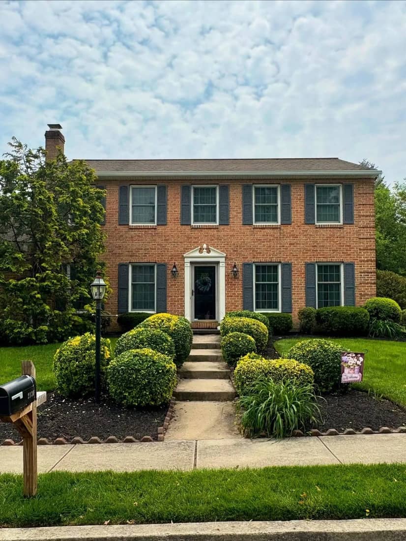 Brick colonial with a walkway, rounded shrubs, and a landscaped front yard