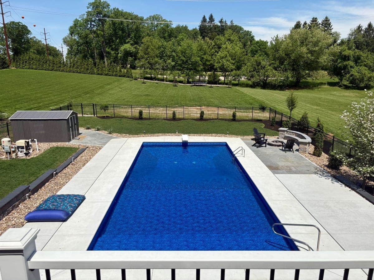 In-ground pool and concrete deck seen from a raised backyard deck