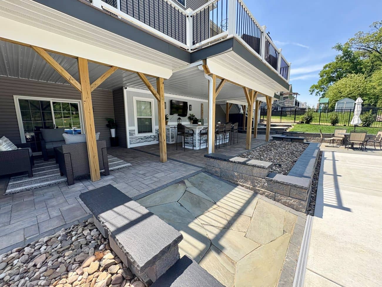 Multi-level patio with covered seating, stonework, wood posts, and decorative gravel beside the yard